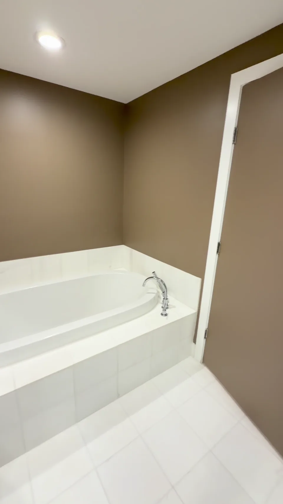 The same bathroom with deeper warm-colored walls beside a white bathtub and trim.