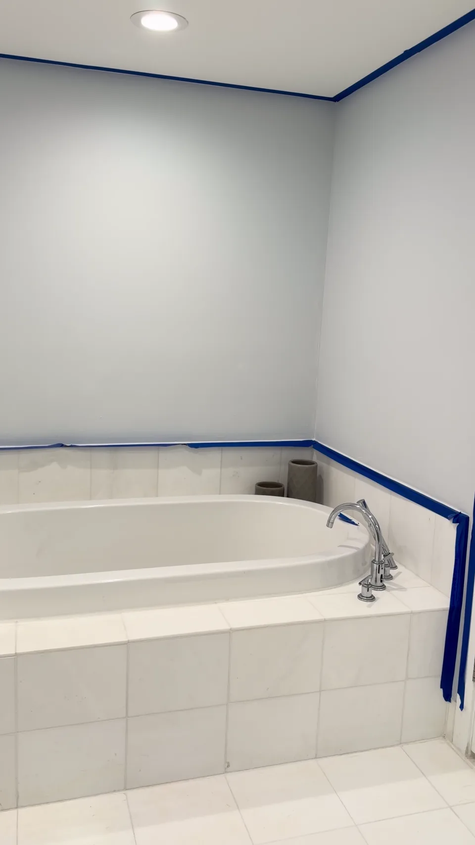 Light bathroom walls and blue masking tape around a white bathtub before repainting.