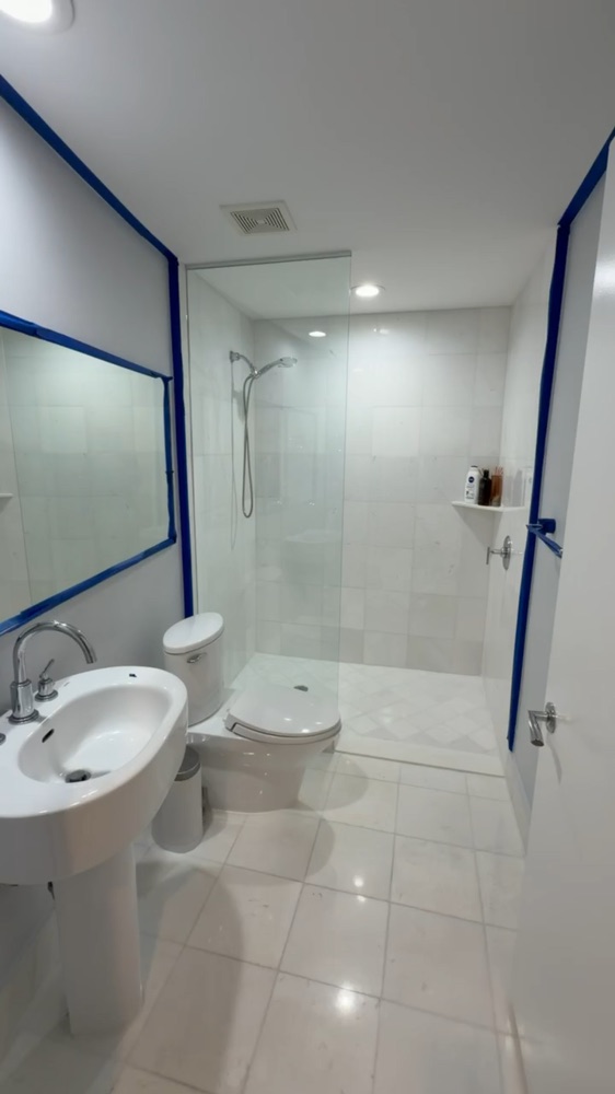 Bathroom with light walls and blue masking tape around the mirror and edges before painting.
